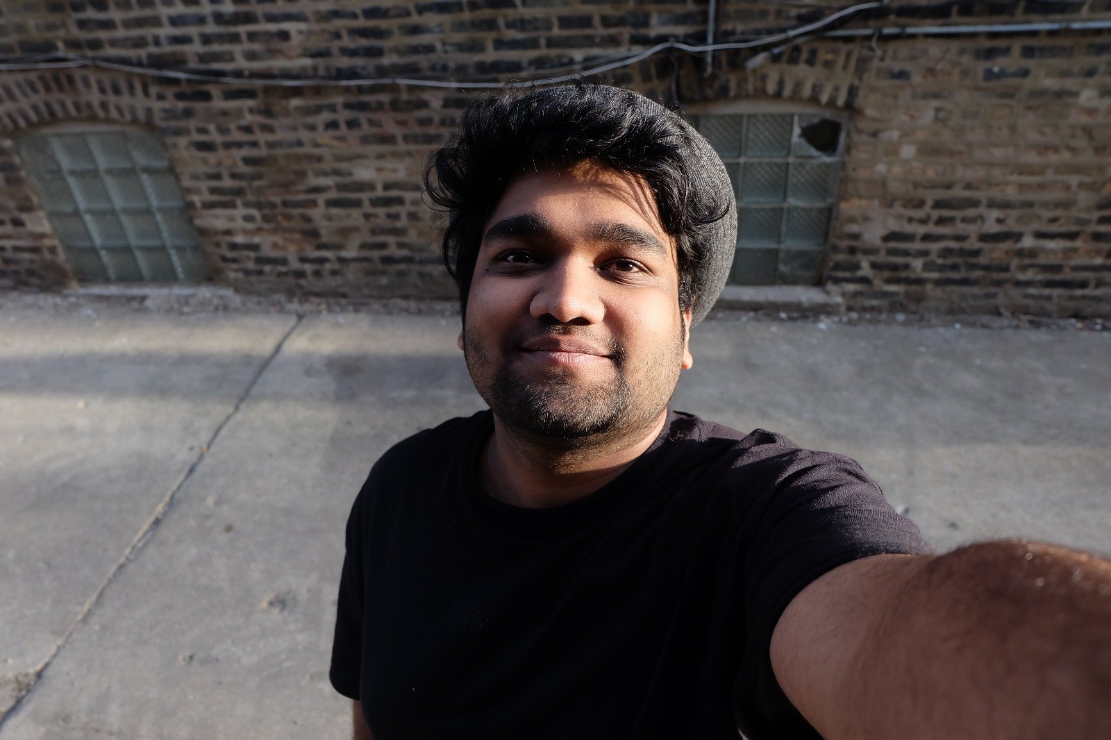 Jeshwanth Srinivasan smiling in a selfie, in front of a brick wall in the sun.