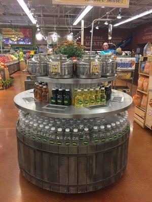 A round bulk-oil display in a grocery store, with steel dispensing tanks above bottled oils.